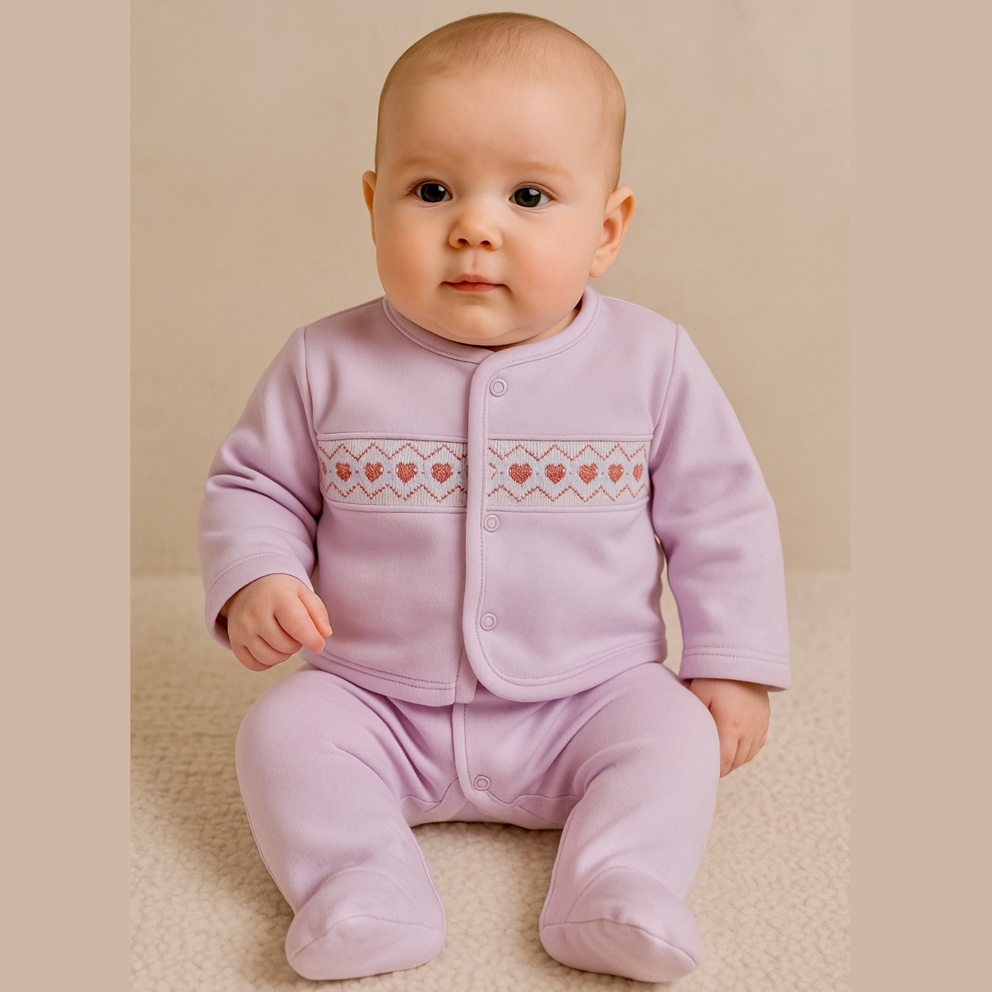 Baby wearing a pink outfit with heart patterns on a beige background