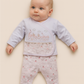Baby wearing a light pink and white outfit with a pattern on a beige background