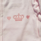 Pink baby outfit with embroidered crown and heart designs on a light pink background