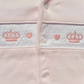 Close-up of a baby outfit with embroidered crowns and hearts on a light pink background.