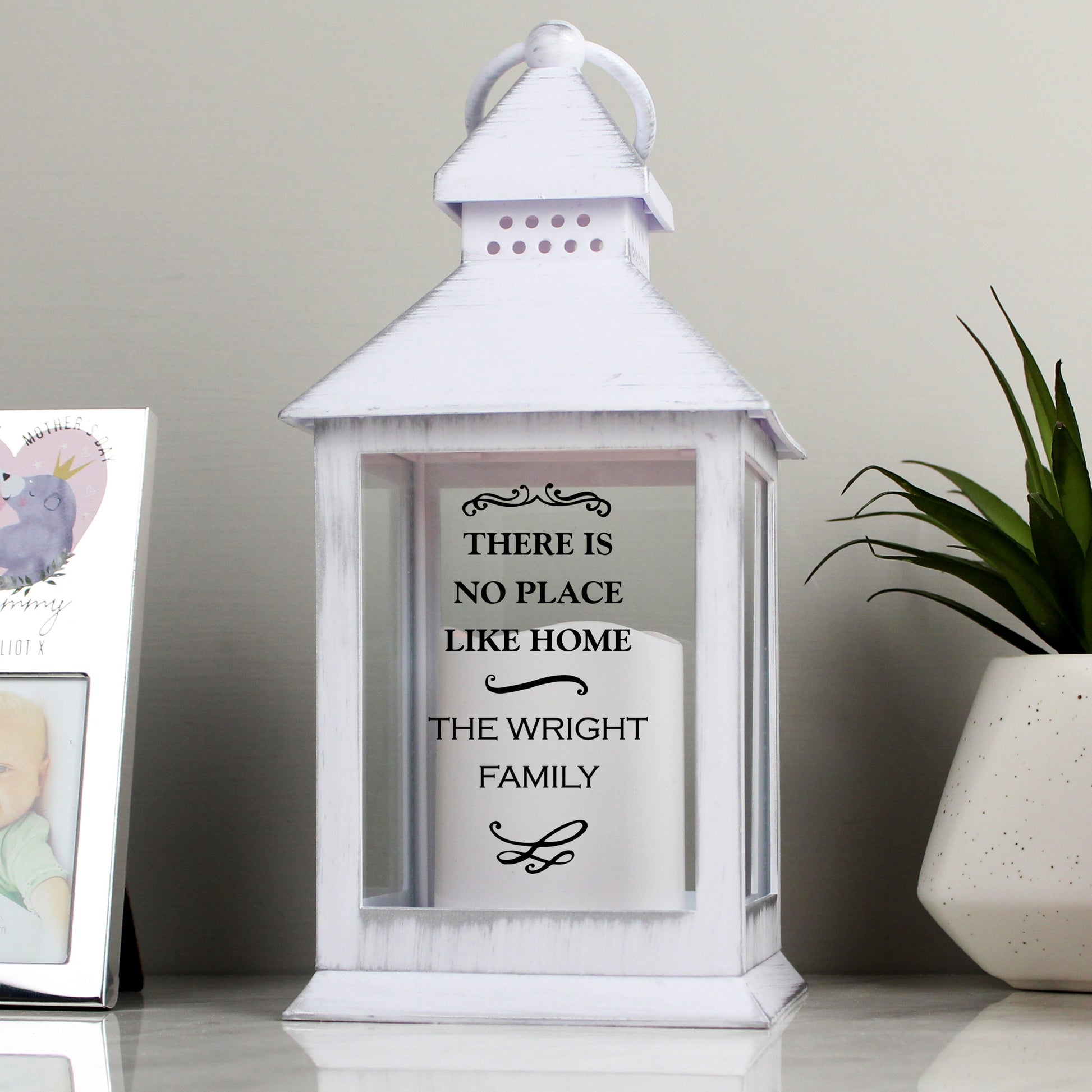 White lantern with black text printed on the front pictured with a potted succulent plant and silver photo frame on a white surface. By Sweetlea Gifts